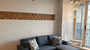 Ein modernes Wohnzimmer mit einem Ecksofa, einem kleinen Sessel und einem Glastisch.