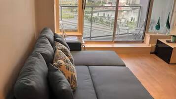 Una sala de estar moderna con un sofá gris, vistas de un paisaje urbano a través de amplios ventanales y una lámpara decorativa.