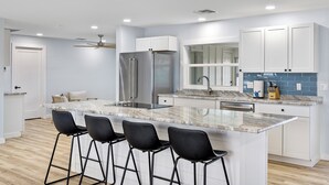 Una cocina moderna con una isla de mármol, taburetes negros, armarios blancos y un refrigerador de acero inoxidable.