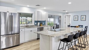 Una cocina moderna con armarios blancos, electrodomésticos de acero inoxidable, una isla de mármol con taburetes y vistas al exterior.