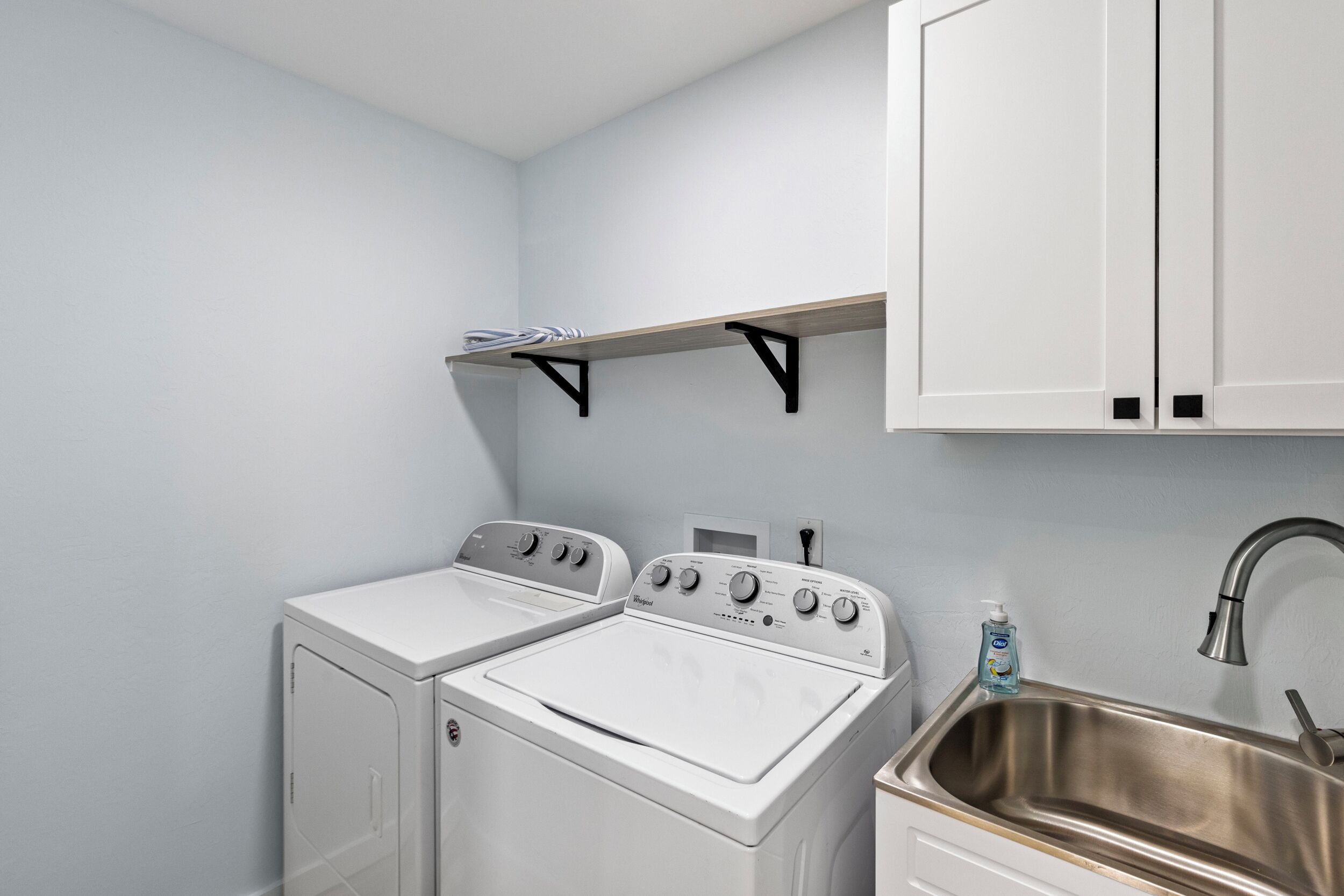 A laundry room with two white front-loading washers and a stainless steel sink.