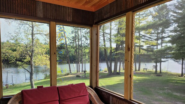 A wicker chair with red cushions in a room with large windows overlooking a lake and trees. - Lakefront Lodging, Beach, Fire Pit, Bar & Grill, Rentals, Live Music, Trails (Tomahawk)