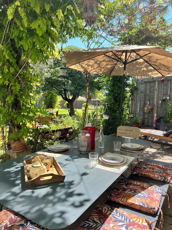 An outdoor dining area with a table set for four, surrounded by greenery and a wooden fence.