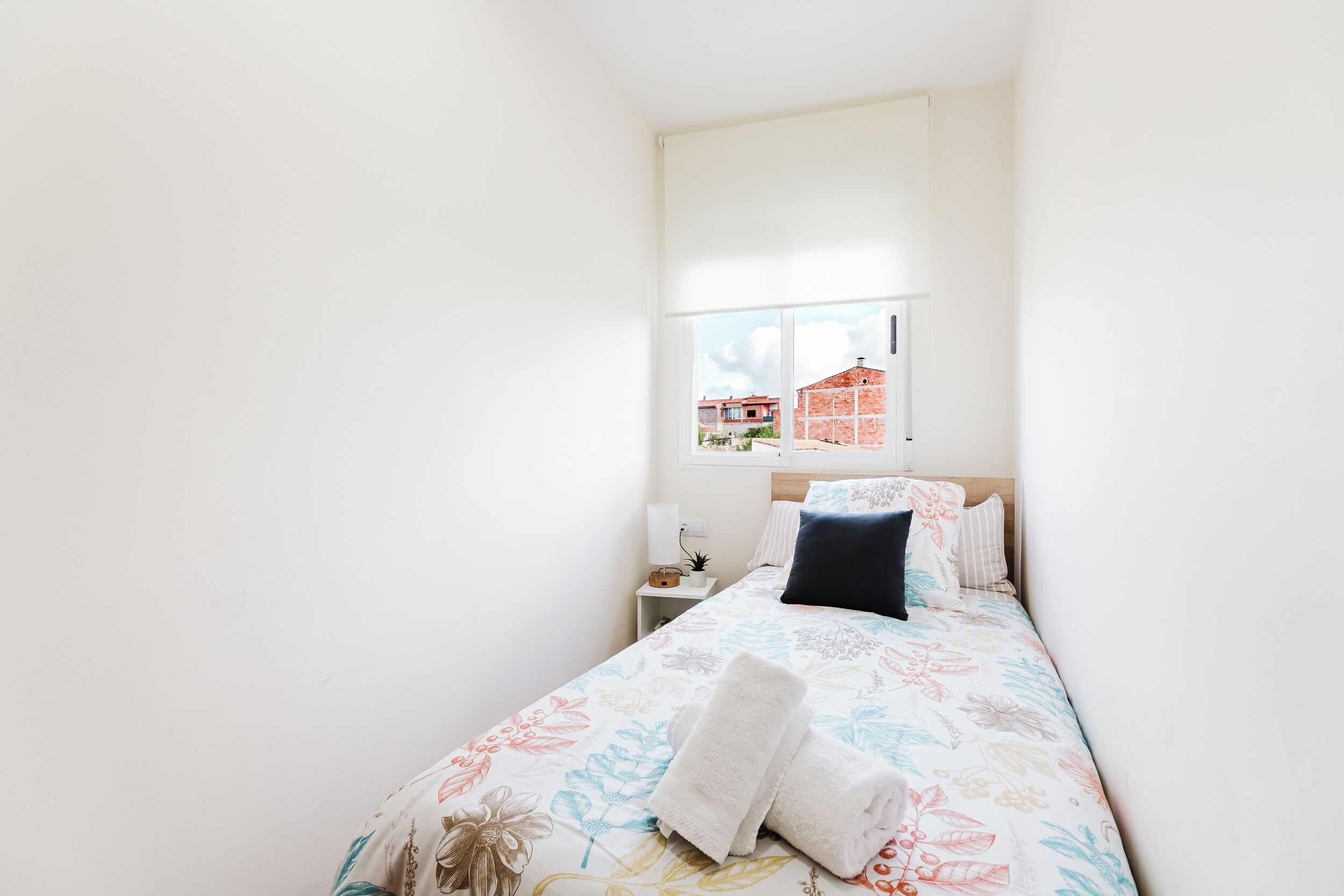 Une chambre à coucher avec un lit, une table de chevet, une fenêtre et une vue sur les bâtiments environnants.