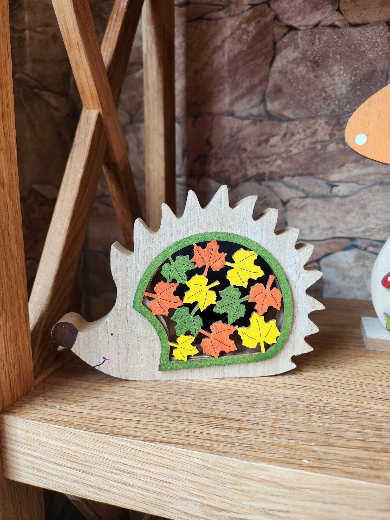 A wooden hedgehog-shaped object with colorful leaves on a wooden surface.