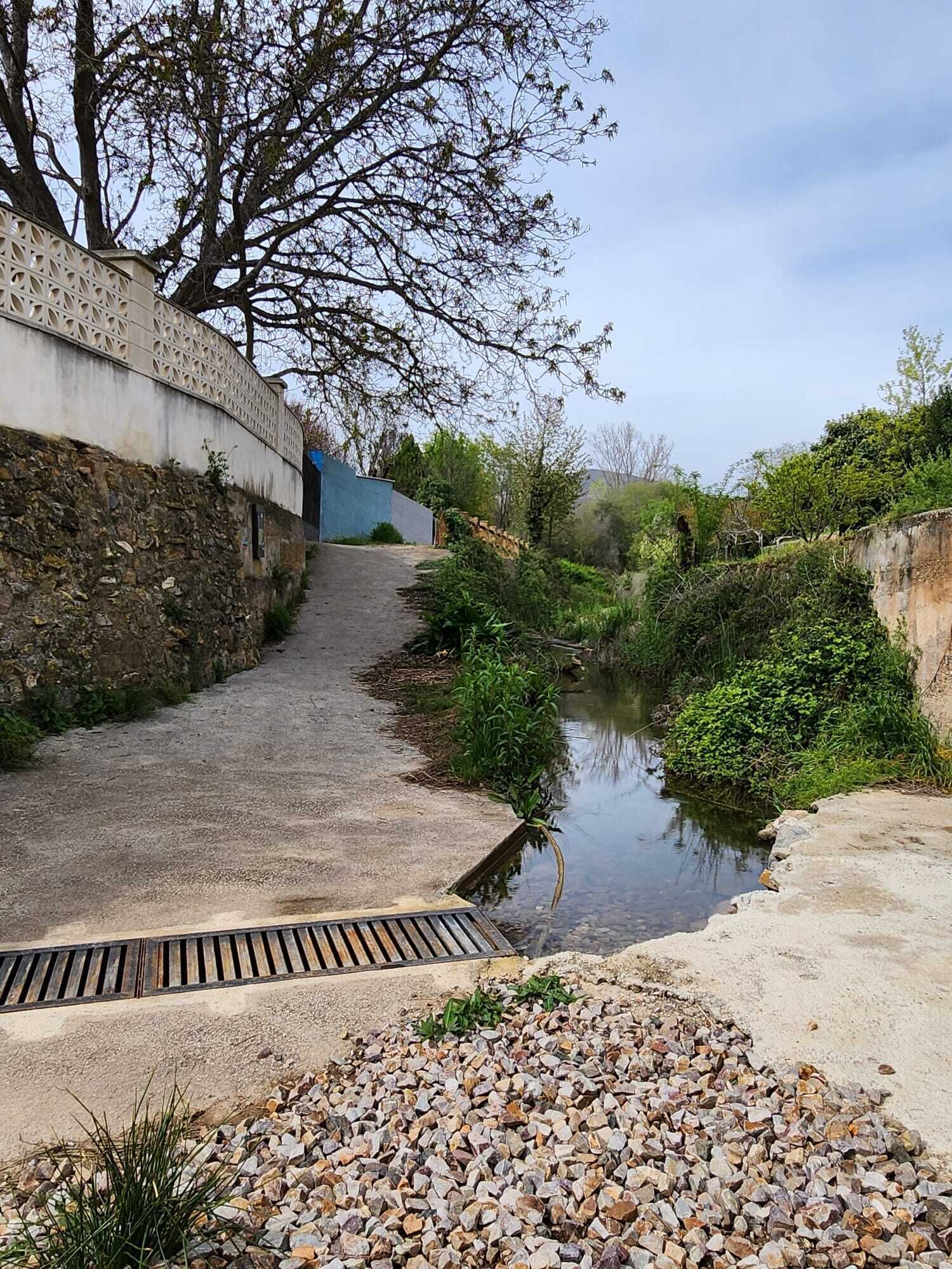 A narrow pathway beside a water channel, with a stone wall on one side and a blue building in the background.