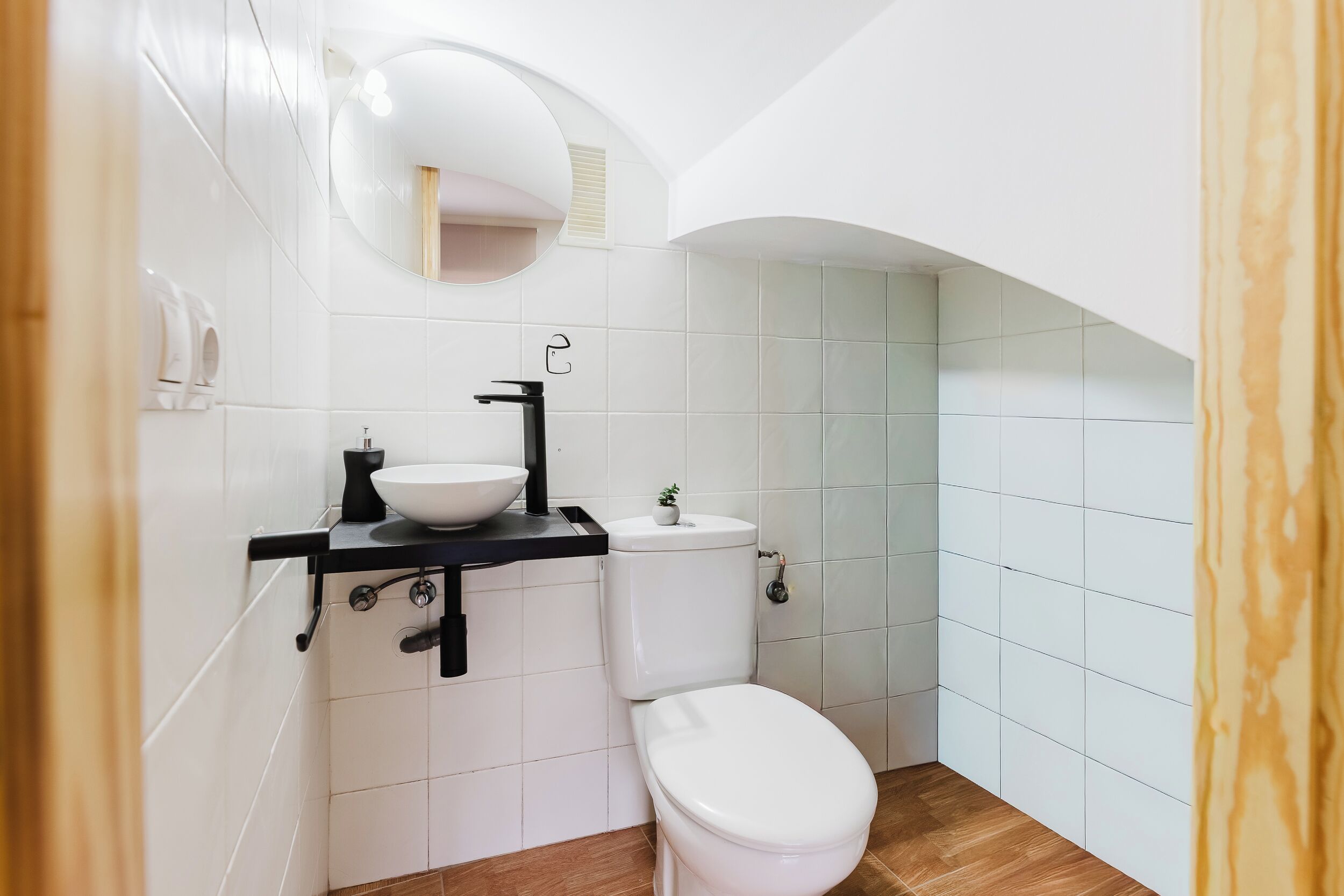 Une petite salle de bain avec des toilettes blanches, un lavabo noir et un petit miroir au-dessus du lavabo.