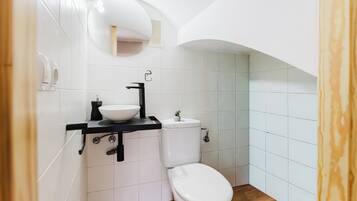 Une petite salle de bain avec des toilettes blanches, un lavabo noir et un petit miroir au-dessus du lavabo.