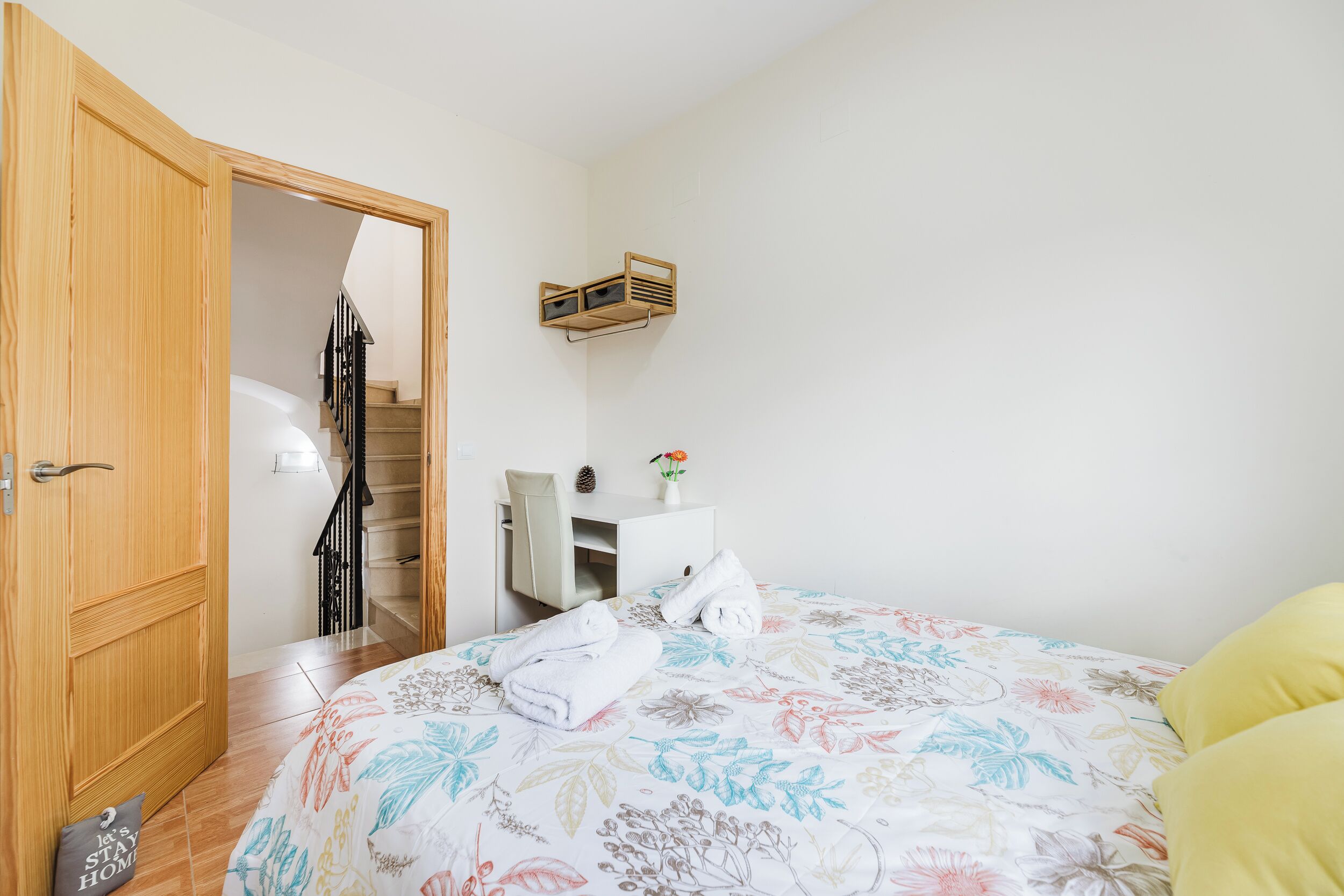 Un dormitorio con una cama, un armario de madera, un escritorio con una silla y una escalera que lleva a otra habitación.