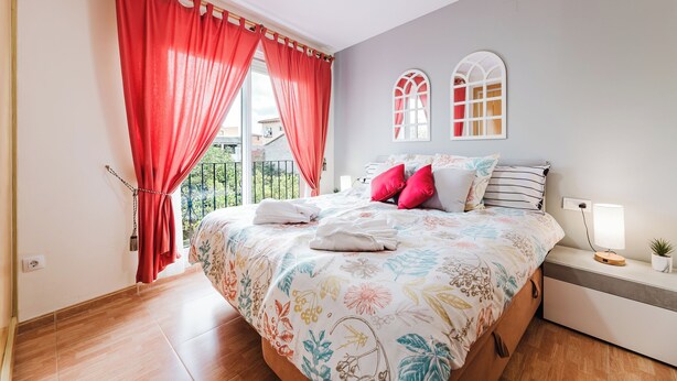 A bedroom with a large bed, red curtains, a nightstand with a lamp, and a view of the outdoors. - Cozy house in the heart of Caudiel, 100 meters from the greenway Ojos Negros. (Caudiel)