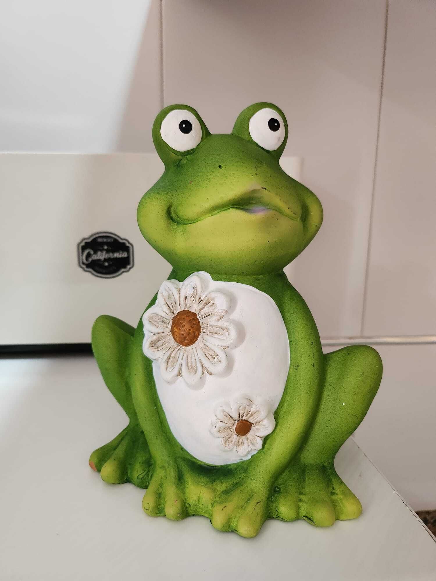 A green frog figurine with white flowers on its chest.