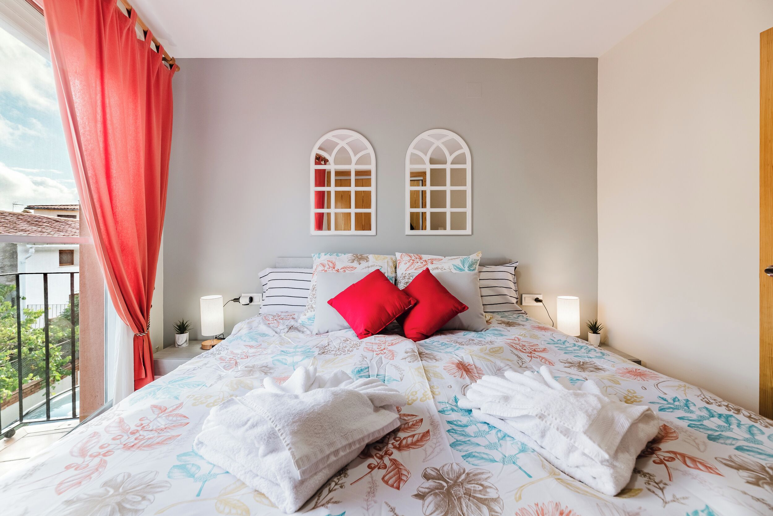Un dormitorio con colcha estampada, dos almohadas rojas, una toalla blanca y vistas al balcón.