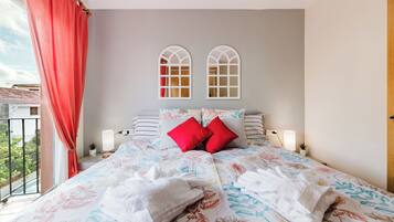 Un dormitorio con colcha estampada, dos almohadas rojas, una toalla blanca y vistas al balcón.