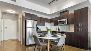 A modern kitchen with dark wood cabinets, stainless steel appliances, and a round dining table with chairs. - Downtown Chic Retreat | Elegant + Free Parking (Calgary)