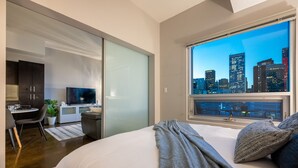 A modern bedroom with a large bed, a city view, a desk, and a sliding door to a balcony. - Downtown Chic Retreat | Elegant + Free Parking (Calgary)