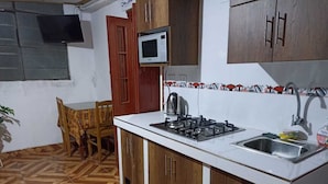 A compact kitchen with a stove, microwave, and sink. There is a dining table with chairs and a potted plant.