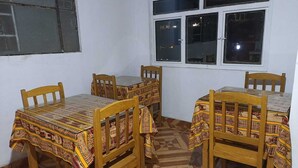 A room with four wooden tables and chairs, each covered with patterned tablecloths. There is a window with multiple panes and a white wall.