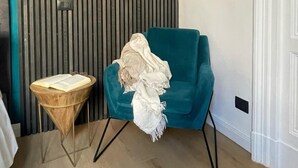A teal armchair with a white throw blanket, a small wooden side table with a book, and a vertical slatted wall with a hanging plant. - Maison Etnea (Catania)