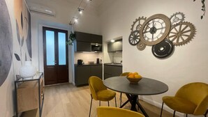 A modern dining area with a round table, yellow chairs, and a wall clock with gears. - Maison Etnea (Catania)