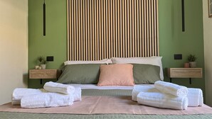 A neatly made bed with green and white bedding, two bedside tables with potted plants, and a vertical wooden slat wall behind the bed. - Maison Etnea (Catania)