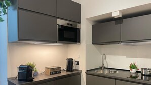 A modern kitchen with dark cabinetry, a built-in oven, a stainless steel sink, and a coffee machine. - Maison Etnea (Catania)