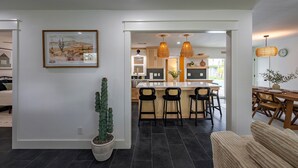 Ein modernes Wohnzimmer mit einer großen Sukkulante, einem gerahmten Kunstwerk und einem Essbereich mit Holzmöbeln und Pendelleuchten.
