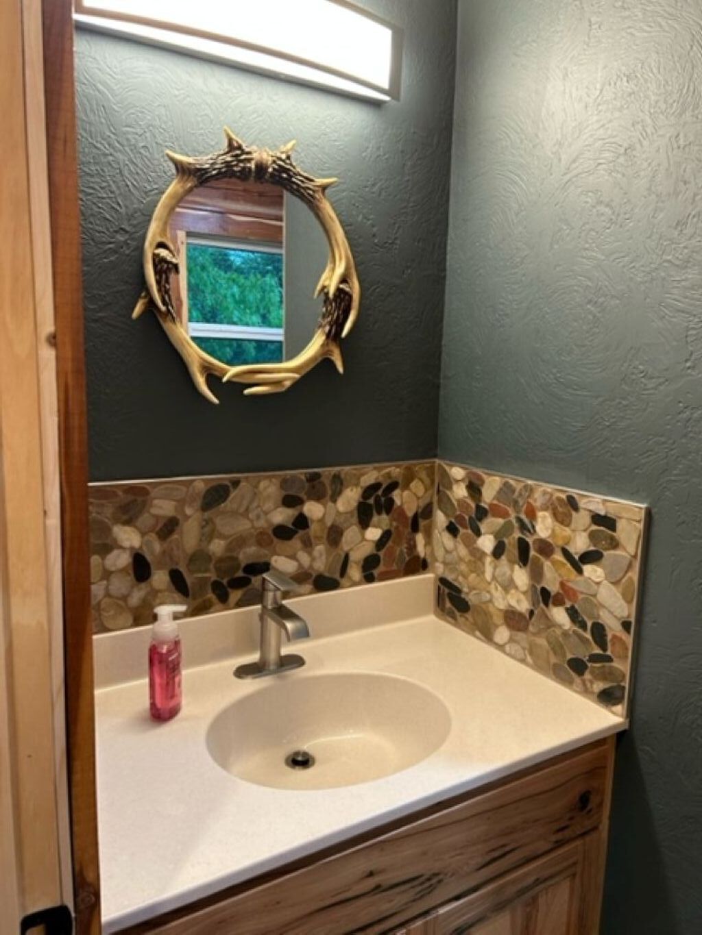 Un bagno con una parete di mosaico in pietra, un lavandino dotato di un moderno rubinetto e uno specchio decorativo a forma di corna.