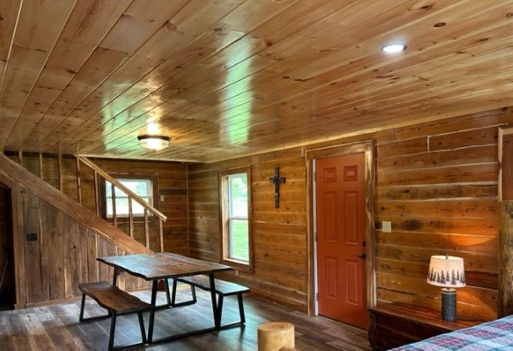 Een houten cabin interieur met een trap, een tafel, een bank, een deur en een lamp.