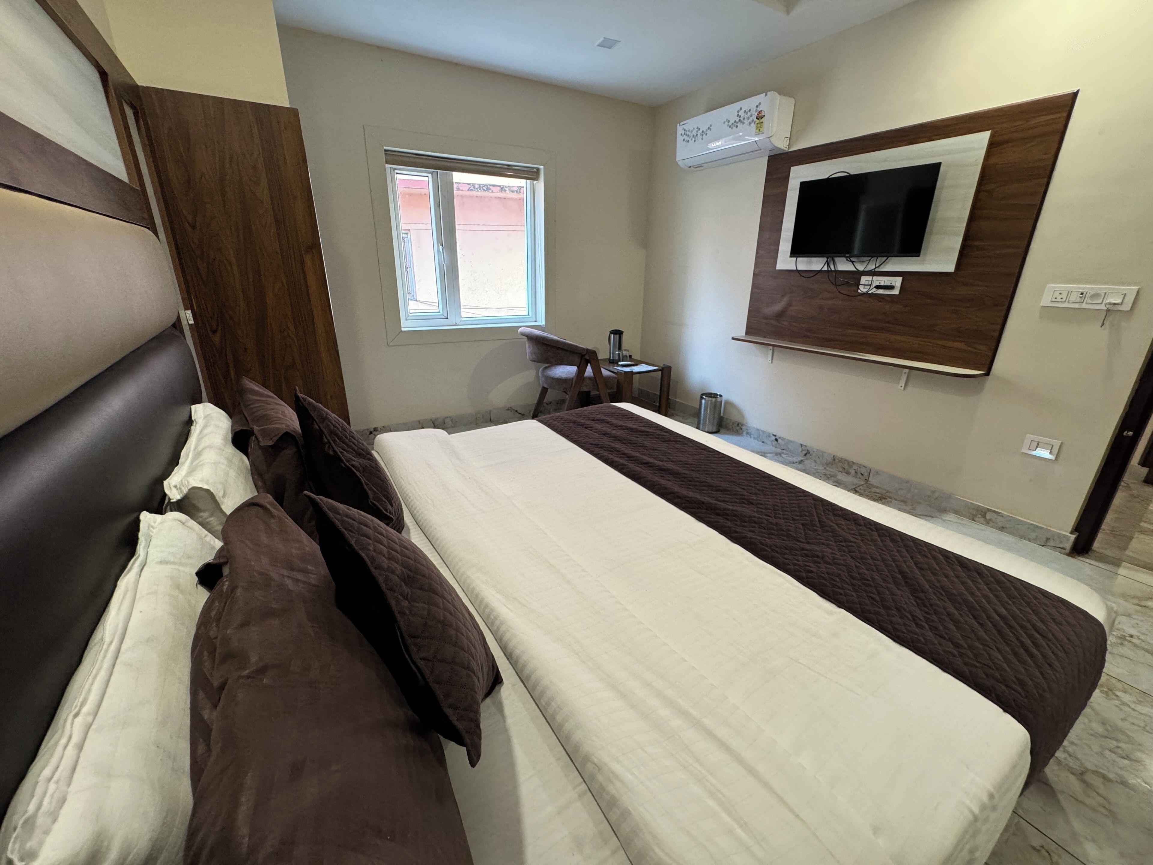 A hotel room with a large bed, a TV mounted on the wall, a window, and a small table with a chair.
