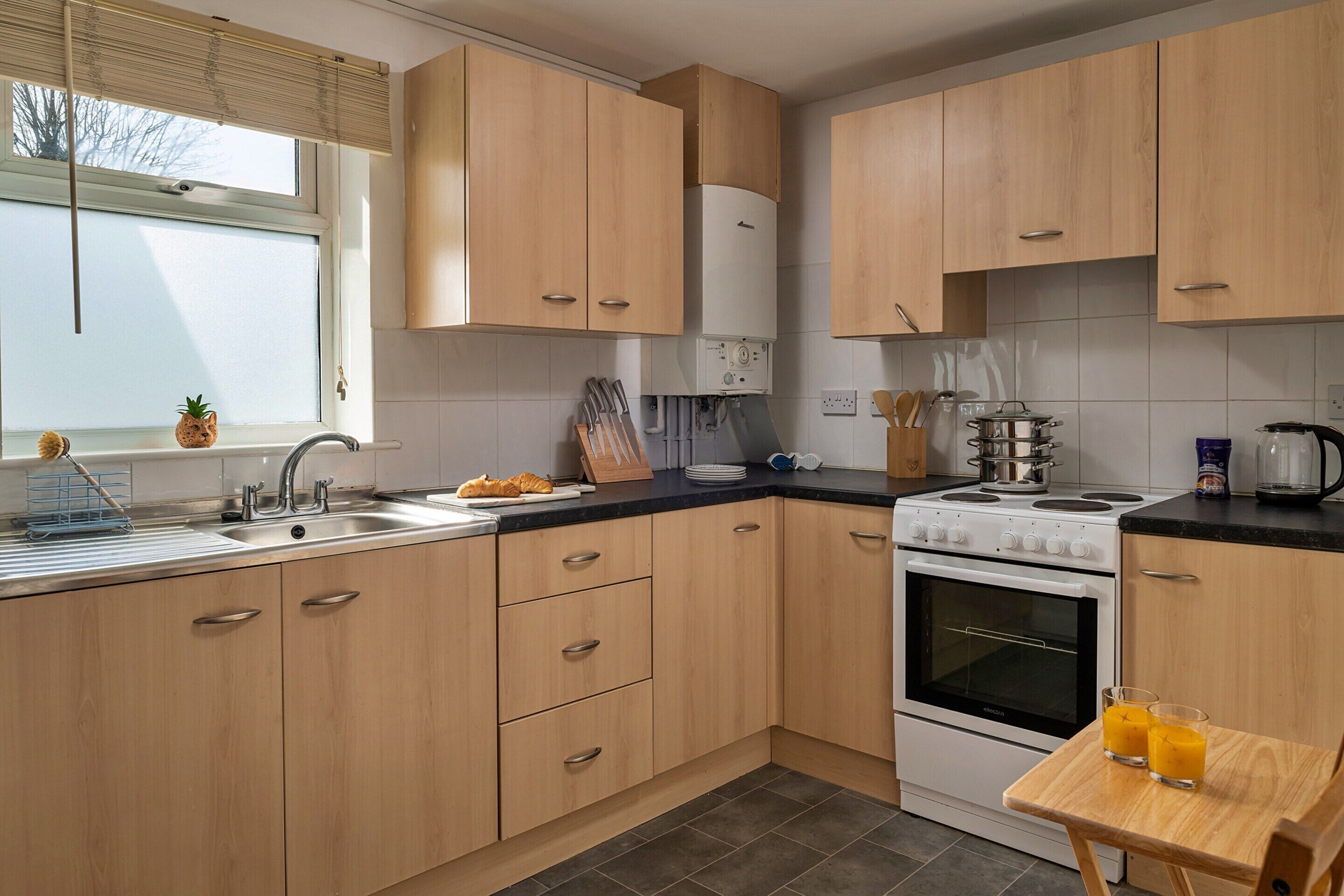 A modern kitchen with wooden cabinets, a stove, a sink, and a table with two glasses of orange juice.