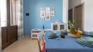 Een eetgedeelte met een blauwe tafelkleed, een fruitmand en een witte kast met een 'Welcome'-bord.