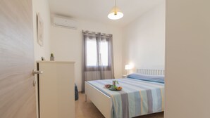 Een slaapkamer met een bed, nachtkastje, lamp, raam met gordijnen en een klein kastje.