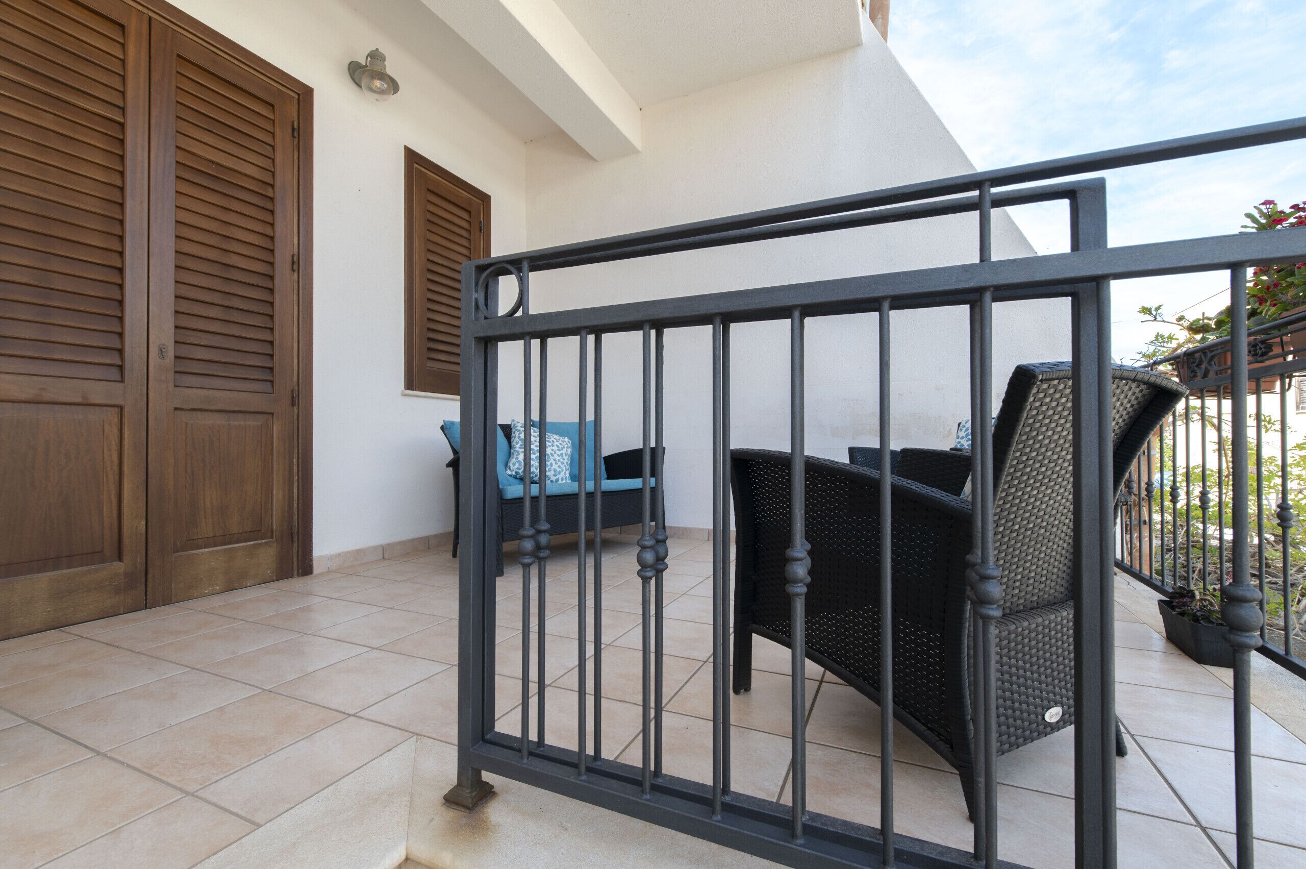 Un balcon avec une balustrade en métal, une chaise en osier et un coussin bleu.