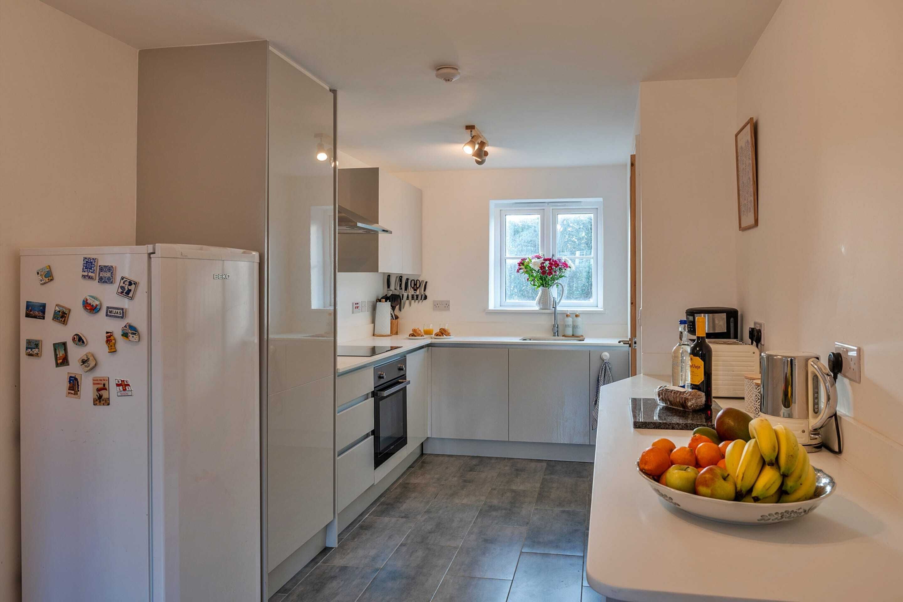 A modern kitchen with a refrigerator, oven, sink, and a bowl of fruit on the counter.