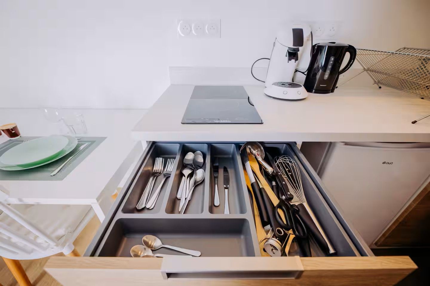 Een keuken met een lade vol keukengerei, een koffiezetapparaat en een waterkoker op het aanrecht.