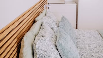 Une chambre à coucher avec une tête de lit en bois, un lit recouvert d’une literie à motifs, une armoire blanche et des œuvres d’art décoratives accrochées au mur.