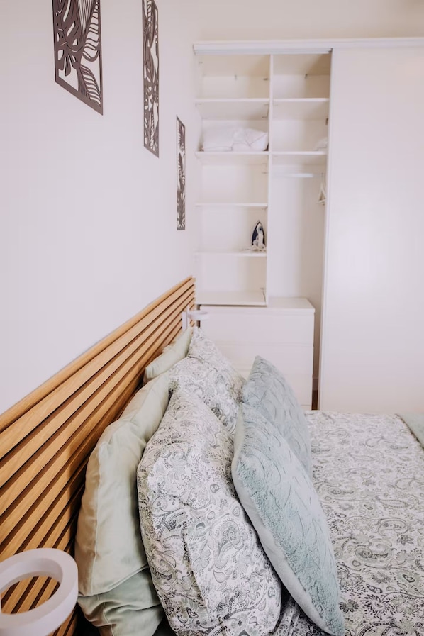 A bedroom with a wooden headboard, a bed with patterned bedding, a white wardrobe, and decorative wall art.