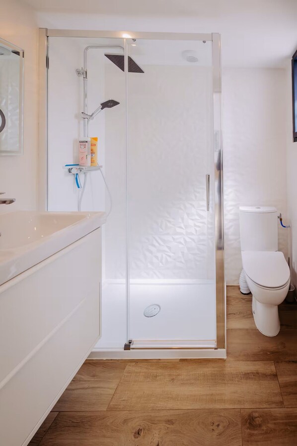 Un baño moderno con ducha acristalada, inodoro y lavamanos.