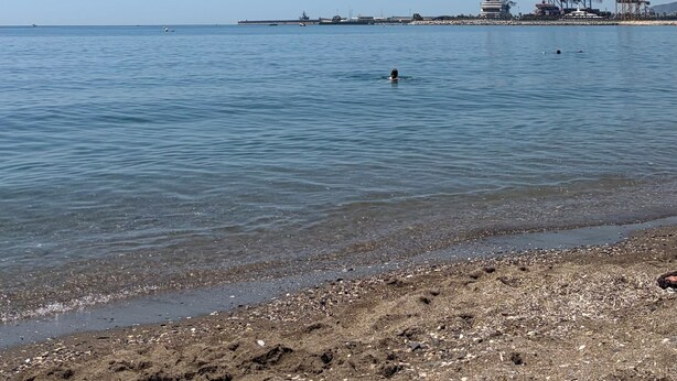 A beach with clear water, a person swimming, and industrial structures in the distance. - Charming relax 2 bedroom apartment 200 meter to beach and 15 min bus city center (Málaga)