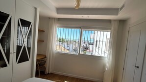Un dormitorio con cama, ventilador de techo, ventana con rejas y vista al exterior.