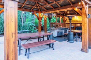 Un patio al aire libre con mesas y bancos de madera, una parrilla y un horno a leña.