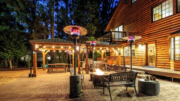 Une cabane en bois dotée d’un patio comprenant un foyer, des sièges d’extérieur et des guirlandes lumineuses.