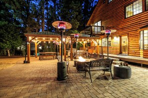 Una cabaña de madera con un patio que cuenta con una fogata, asientos exteriores e iluminación colgante.