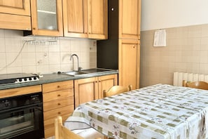 Une cuisine dotée de meubles en bois, d’un four encastré, d’un évier et d’un coin repas avec une table et des chaises.