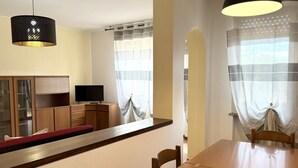 Un coin repas avec une table et des chaises en bois, un téléviseur posé sur un meuble et un luminaire suspendu.