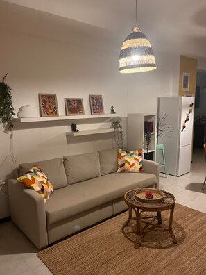 Relax in this inviting living space with a beige sofa, armchair, and pendant light, surrounded by artwork and a potted plant.