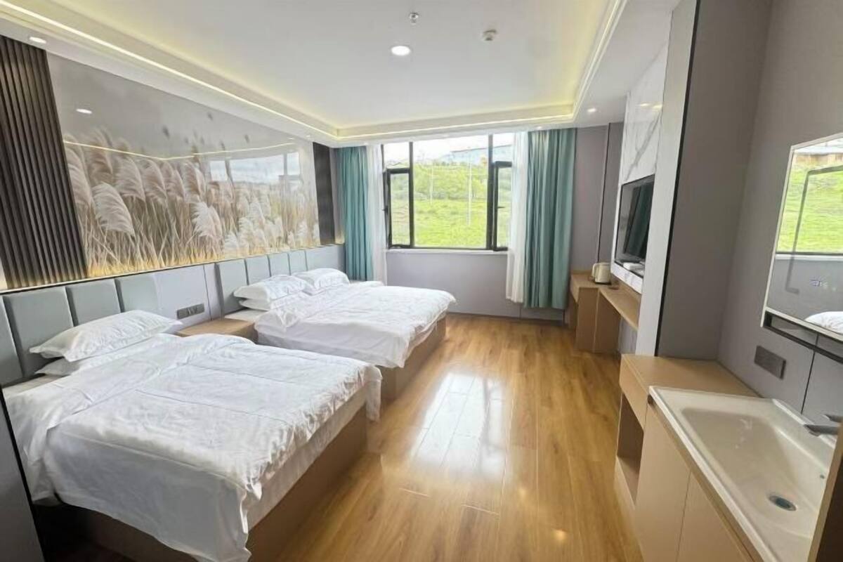 A hotel room with two beds, a TV, a large window, and a view of greenery.