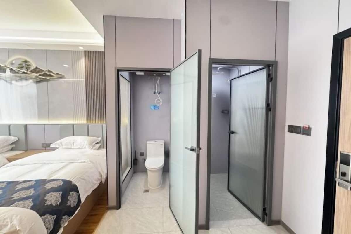 A modern hotel room with a bed, a bathroom with a toilet and shower, and a glass partition between the two.