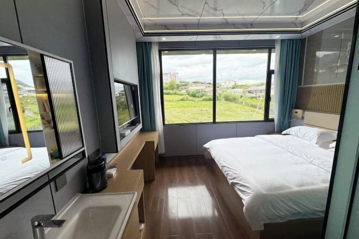 A modern hotel room with a large bed, a TV, a built-in bench, and a view of the outdoors.
