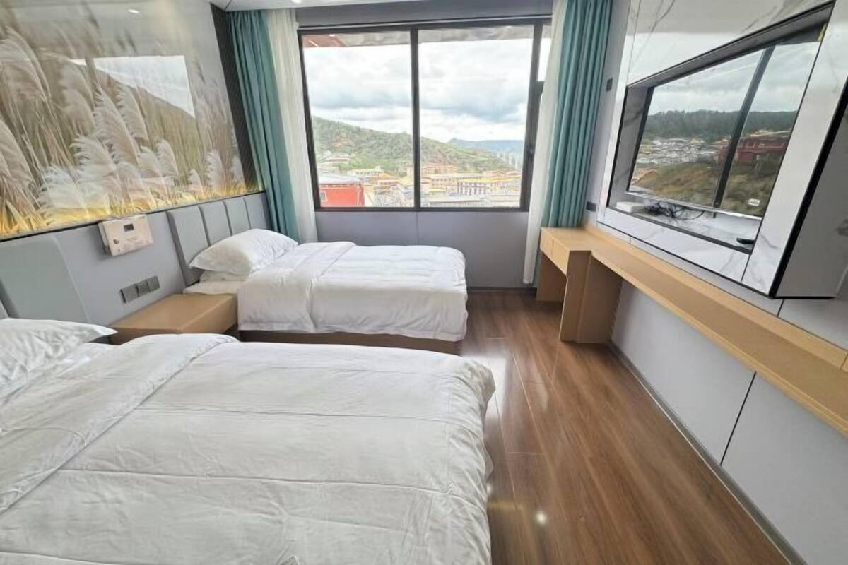 A hotel room with two beds, a large window with a view, a wooden desk, and a wall-mounted TV.
